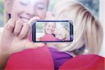 Hand holding smartphone showing against happy mother and daughter on the couch with heart card