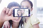 Hand holding smartphone showing against cute mother and daughter smiling at camera