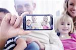 Hand holding smartphone showing against portrait of a smiling family sitting on sofa