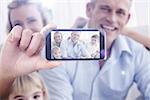 Hand holding smartphone showing against happy family relaxing on the couch