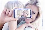 Hand holding smartphone showing against mother sitting on the couch with her daughter kissing her cheek