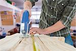 Carpenter cutting wooden plank with electric saw against workshop