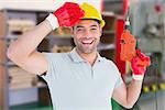 Smiling manual worker holding drill machine against workshop