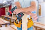 Midsection of male carpenter with power drill and plank against workshop