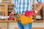 Midsection of handyman holding spirit level against workshop