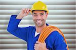 Confident repairman wearing hard hat while holding wire roll against grey shutters