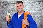 Smiling electrician with rolled wire and multimeter against grey brick wall
