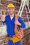 Male technician with wire roll gesturing thumbs up against red brick wall