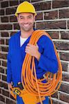 Smiling handyman with rolled wire on white background against red brick wall