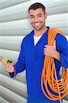 Smiling electrician with wire roll and multimeter against grey shutters