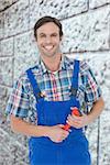 Confident plumber holding monkey wrench against grey brick wall