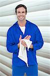 Confident mechanic wiping hand with napkin against grey shutters