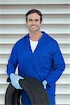 Confident mechanic holding tire against grey shutters