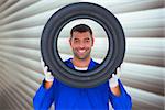 Happy mechanic looking through tire against grey shutters