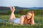 Young woman lying on grass in a meadow at sunset in spring, Germany