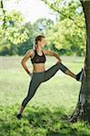 Close-up of a young woman exercisng, stretchnig using a tree in a park in spring, Bavaria, Germany