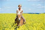 Close-up of young woman riding a Haflinger horse in a canola field in spring, Bavaria, Germany