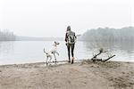 Young woman throwing stick for her dog on misty lakeside