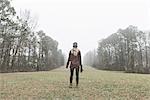 Rear view of young female photographer standing in misty field