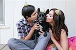 Young couple kissing dog on cheek and wearing party hats