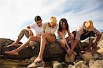 Group of friends sitting together on rocks on beach, looking in rock pools