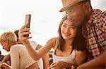 Young couple taking self portrait on beach, using smartphone