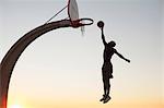 Young man with basketball, jumping towards net, outdoors