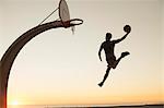 Young man with basketball, jumping towards net, rear view, outdoors