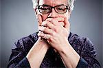 Studio portrait of mature businessman with hands covering mouth