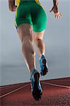 Rear waist down view of young female athlete running on race track