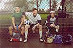 Portrait of three male soccer players sitting behind wire fence