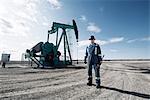 A man in overalls and a hard hat with a large wrench working at an oil extraction site.