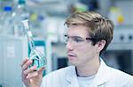 Male scientist holding up and looking at flask in lab