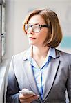 Mature businesswoman with smartphone gazing out of office window