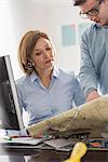 Young businessman looking at blueprint with architect at office desk