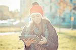 Mid adult woman in red pom pom hat using digital tablet in park