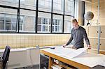 Male designer looking at blueprint in creative office