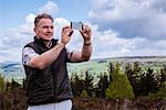 Male hiker photographing with smartphone on heather moors, Pateley Bridge, Nidderdale, Yorkshire Dales