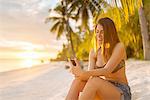 Young woman using smartphone on Anda beach, Bohol Province, Philippines