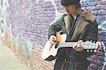 Musician playing guitar by canal wall, Milan, Italy