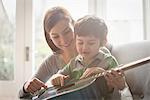 Boy sitting on mother's lap and learning to play guitar