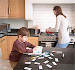 Boy coloring in book on kitchen counter as mother prepares dinner