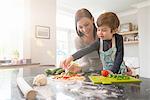 Mother and son preparing pizza together in kitchen