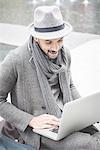 Smiling businessman sitting on wall using laptop