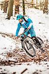 Young male mountain biker speeding on snow covered forest track