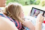 Daughter sitting on mother's lap using digital tablet