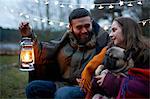 Young camping couple with dog wrapped in blanket