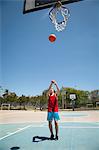 Young male basketball player throwing ball toward basketball hoop