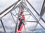 Tower workers climbing radio tower on offshore windfarm, low angle view