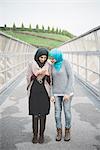 Two young female friends reading smartphone texts on park footbridge